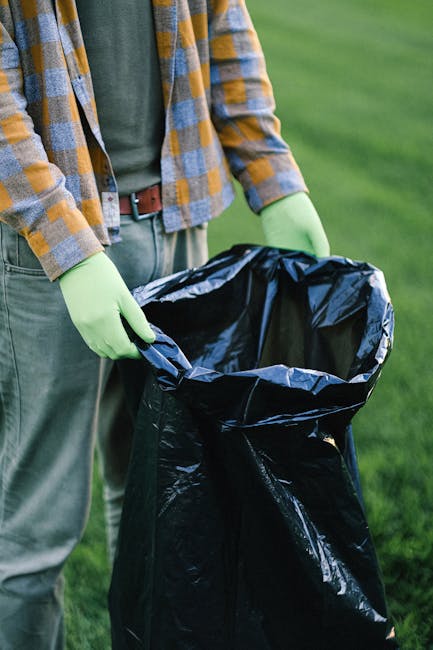 A pile of mixed household waste, including discarded cardboard boxes of various sizes, some flattened and others partially crushed, along with plastic wrapping and paper bags, rests against a rough, t